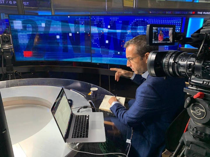 Elliott Gotkine preparing at a broadcast studio desk beside a television camera